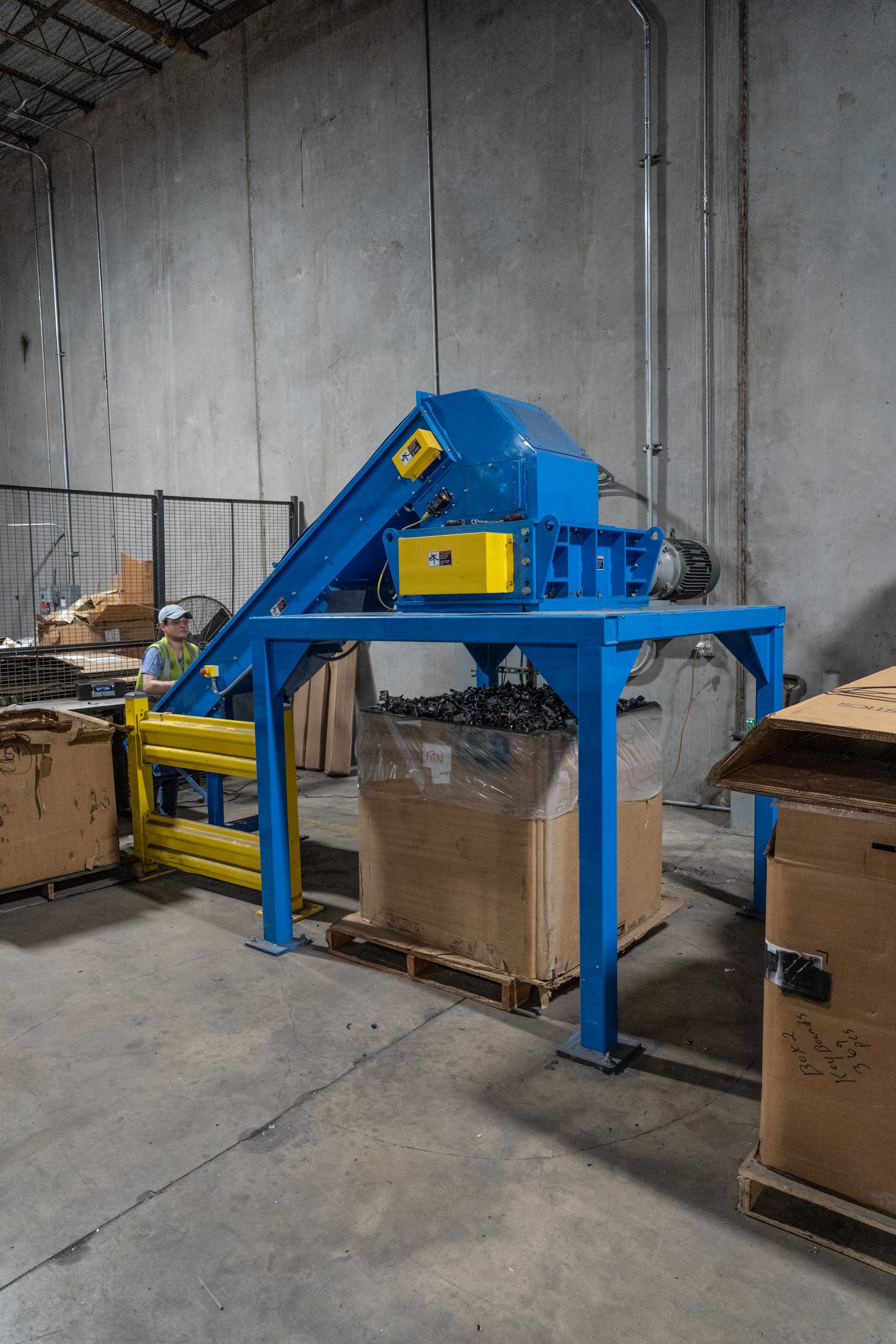 Workers operating heavy machinery on a factory floor shredding hard drives, cds and data bearing media